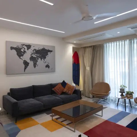 Living room with a charcoal three-seater under a grey world-map canvas, two tan swivel lounge chairs against the sheer-curtained window wall