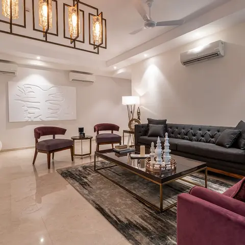 Living room with a charcoal tufted sofa and maroon velvet armchairs around a black-and-brass glass coffee table