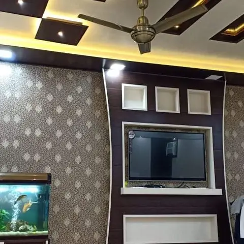Living room with a checkerboard-pattern cove-lit false ceiling, damask wallpaper, a dark wood TV feature unit with display niches, and a fish tank on a stand.