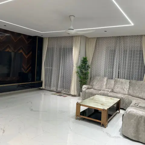Living room with a chevron-pattern dark wood TV wall, a grey suede-style sectional sofa, and a marble-and-brass coffee table under a cove-lit ceiling.
