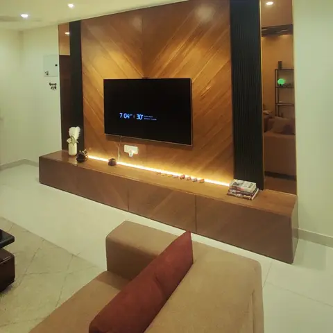 Living room with a chevron-pattern wood TV panel wall lit by an under-shelf light profile, flanked by mirror panels