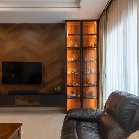 Living room with a chevron-pattern walnut veneer TV wall, a floating dark-wood TV console, a black-framed backlit glass display cabinet styled with curios