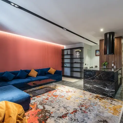 Living room with a coral accent wall lit by a cove backlight, a navy blue sectional sofa styled with mustard cushions, a patterned area rug