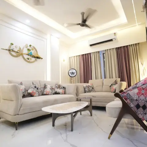 Living room with a cove-lit stepped POP ceiling, panelled accent wall with a gold wall sculpture, beige tufted sofas and a floral wingback chair