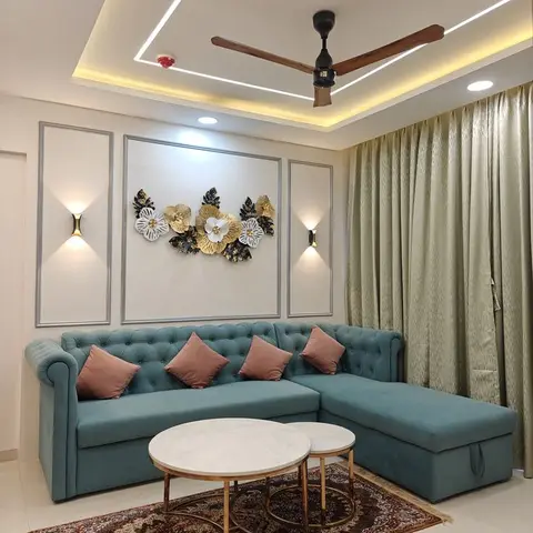 Living room with a cove-lit false ceiling and ceiling fan, a teal tufted chesterfield-style L-shaped sofa with blush cushions