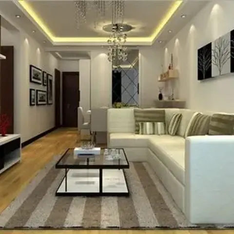 Living room with a cove-lit ceiling and crystal chandelier over a cream sectional sofa, glass coffee table, and a wall-mounted TV on a floating console.