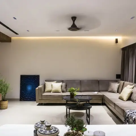 Living room with a cove-lit false ceiling, a fluted wood-panelled TV wall, a large taupe L-shaped sectional sofa, and layered black nesting coffee tables.
