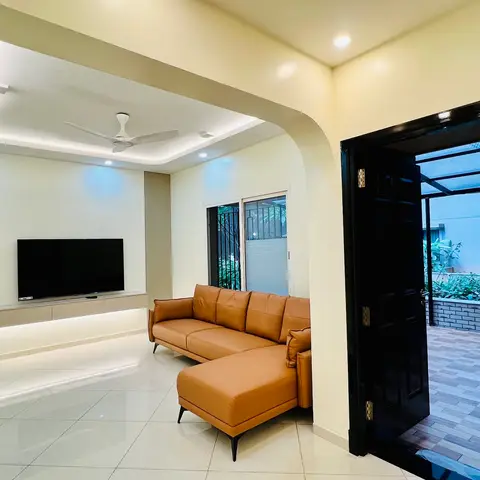 Living room with a cove-lit pop ceiling arch, floating white TV console, tan leather sectional sofa, and a glossy black main door opening to an outdoor patio.