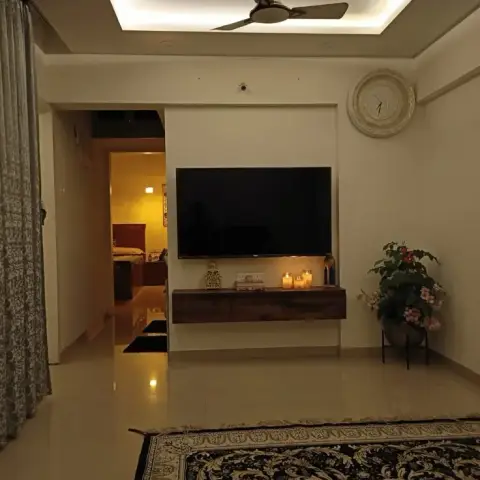 Living room with a cove-lit ceiling and ceiling fan, a wall-mounted TV on a floating wood console styled with candles, a round textured wall clock