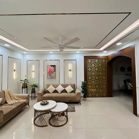 Living room with a cove-lit stepped false ceiling, panel-moulded walls, taupe fabric sofas around nested marble coffee tables