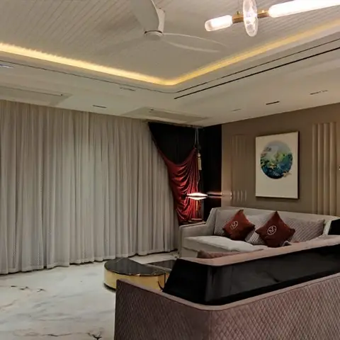 Living room with a cove-lit tray ceiling, floor-to-ceiling sheer curtains with a draped red velvet panel, a quilted grey sofa