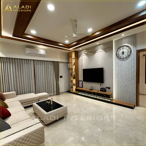 Living room with a cream L-shaped sofa and quilted ottomans facing a marble-slab TV feature wall with a pebble-lit floating unit