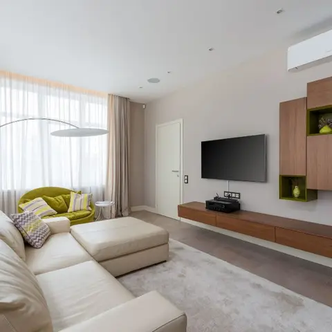 Living room with a cream leather sectional sofa, a mustard accent armchair and a floating walnut TV unit with green-lined display cubbies