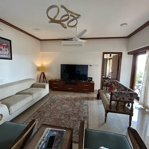 Living room with a cream sofa, cane armchairs, a floral-upholstered bench, and a sculptural gold pendant light over a patterned area rug
