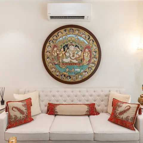 Living room with a cream tufted sofa styled with red tasselled cushions beneath a round Tanjore-style Ganesha painting