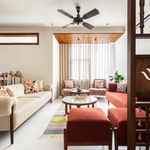 Living room with a cream tufted-arm sofa and floral cushions, a carved wood jaali partition with hanging brass bells and lotus cut-out