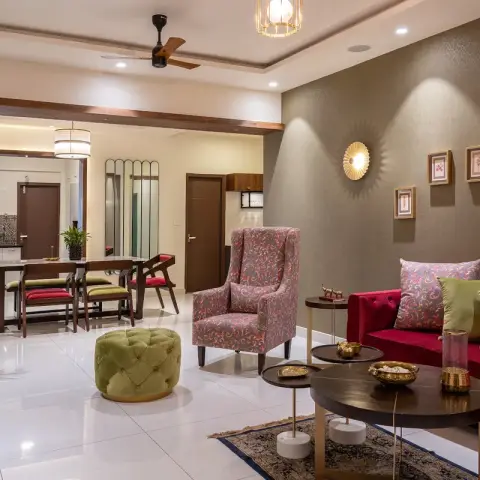 Living room with a crimson velvet sofa against an olive textured wallpaper wall, a brass sunburst sconce among five small botanical prints above it