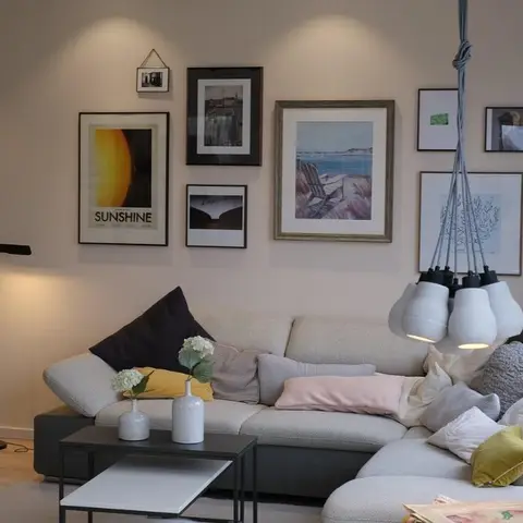 Living room with a curated gallery wall of framed prints above a grey sectional sofa and a cluster of cocoon-shaped pendant lights