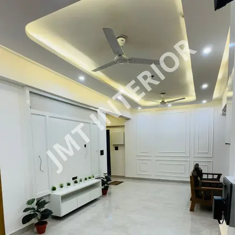 Living room with a curved cove-lit false ceiling holding two fans, a white panelled feature wall, and a white TV console lined with small potted plants