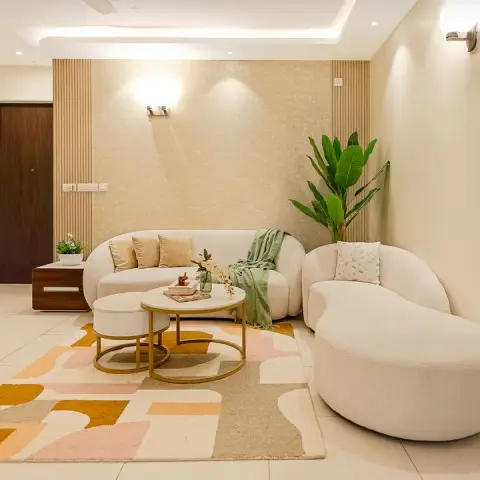 Living room with a curved cream boucle sofa and matching chaise on a blush-and-mustard abstract block rug, two brass-frame nesting tables in front