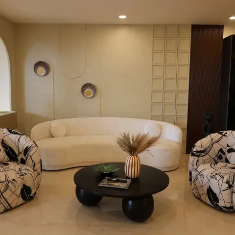 Living room with a curved cream boucle sofa flanked by black-and-white graphic-print swivel armchairs, a round black pedestal coffee table