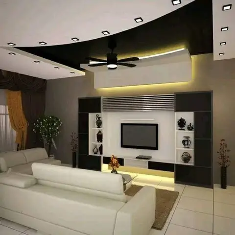 Living room with a curved multi-level POP false ceiling with cove lighting over a black-and-white TV unit fitted with lit display niches for decorative vases