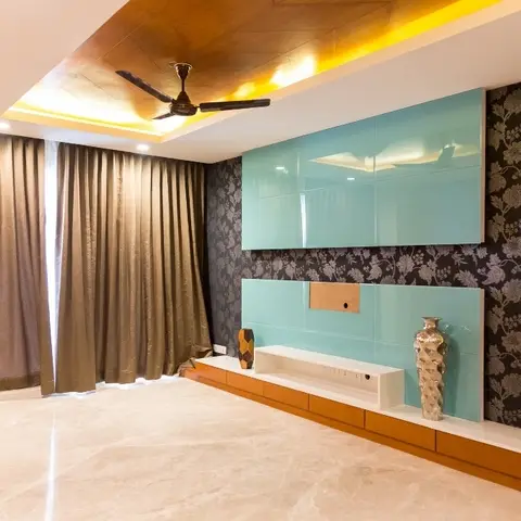 Living room with a dark floral wallpaper feature wall, glossy teal lacquer TV unit on an amber-lit wood cove ceiling, and floor-length bronze curtains.