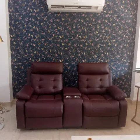 Living room with a dark floral wallpaper accent wall, a maroon leather reclining loveseat with a center console