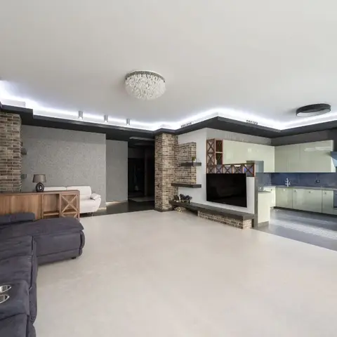 Living room with a dark grey sectional sofa facing a brick-clad TV feature wall, open kitchen visible beyond
