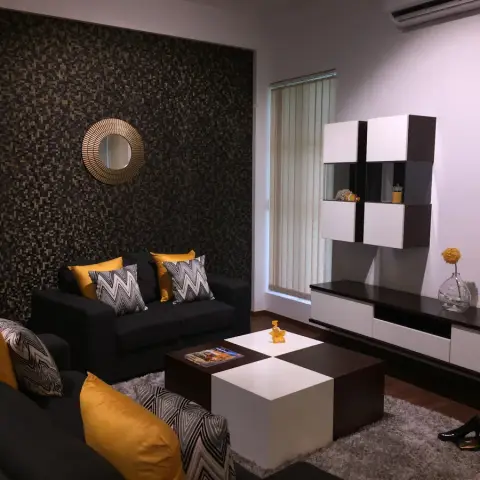 Living room with a dark mosaic-tile feature wall and a sunburst mirror, charcoal sofas dressed in mustard and chevron cushions