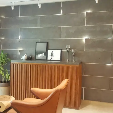 Living room with a dark textured stone-slab accent wall lit by track spotlights, a wood-slat console styled with framed bird prints, and tan leather armchairs.