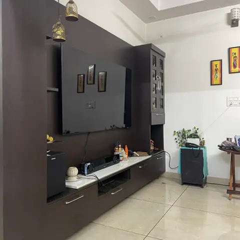 Living room with a dark wenge TV unit wall styled with framed tribal folk-art paintings and decorative hanging bird-cage lanterns.