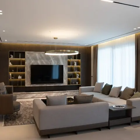Living room with a dark wood-veneer TV wall framing a backlit marble slab and open display shelving, a brass ring pendant light