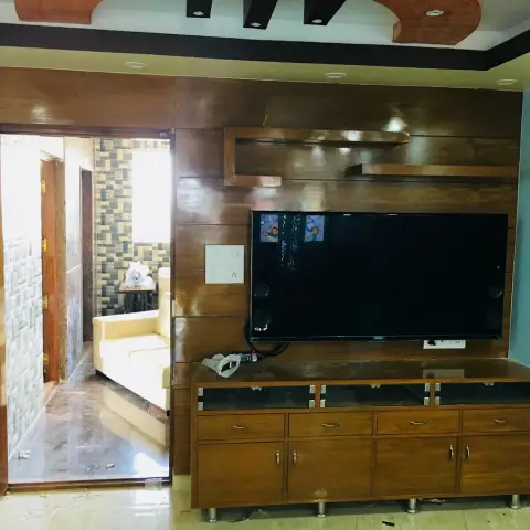 Living room with a dark wood-panelled TV feature wall beneath an orange-and-black cove pop ceiling, main door opening into a mosaic-tiled entrance hallway.