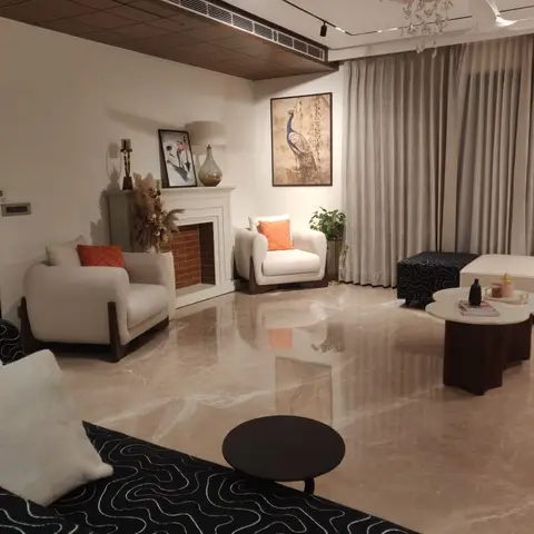 Living room with a decorative fireplace mantel, wood-clad cove-lit ceiling coffer, a floral crystal chandelier, and polished marble flooring.