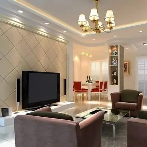Living room with a diamond-quilted padded panel TV wall, a multi-arm chandelier under a cove-lit ceiling, brown armchairs around a glass coffee table