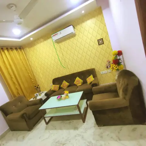 Living room with a diamond-textured yellow 3D wall panel behind a brown velvet tufted sofa set, matching yellow silk curtains, and a glass-top coffee table.