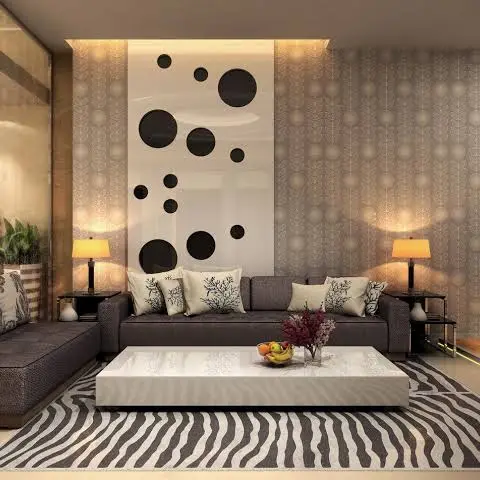 Living room with a dot-pattern art panel on a cove-lit feature wall, a dark brown sectional sofa, and a zebra-print rug beneath a white lacquer coffee table.