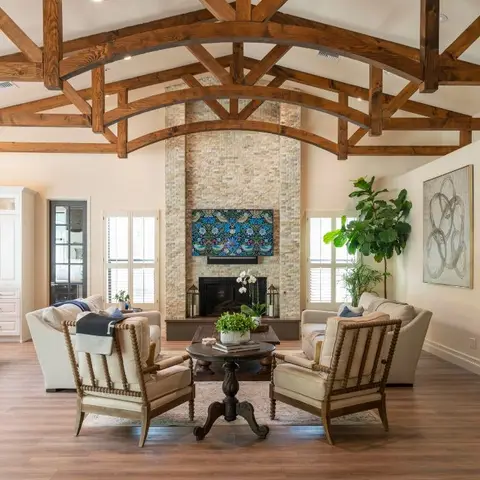 Living room with a dramatic arched wood-truss vaulted ceiling, a stacked-stone fireplace with a colorful art panel