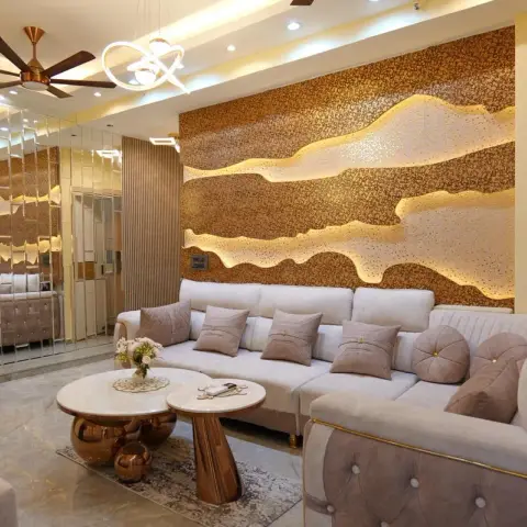 Living room with a dramatic backlit textured gold-bronze feature wall behind tufted grey sofas with gold piping, and a mirrored wall panel divider.