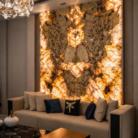 Living room with a dramatic backlit amber onyx stone feature wall, a beige sofa styled with navy and beige cushions, a brass waterfall coffee table