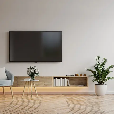 Living room with a floating wood-veneer TV console lit by warm cove lighting, a fluted wood accent wall, herringbone wood flooring, and a blue tufted armchair.