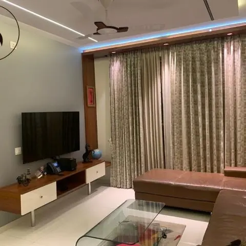 Living room with a floating wood TV console, patterned floor-to-ceiling curtains, a brown leather sectional and a cove-lit ceiling with blue LED accent.