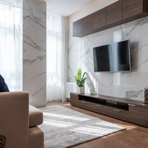 Living room with a floor-to-ceiling marble slab wall behind a wall-mounted TV, a walnut floating console and overhead cabinet