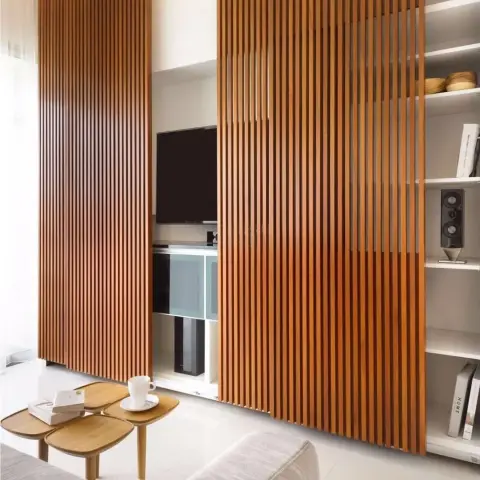 Living room with a floor-to-ceiling sliding fluted-wood slat screen that conceals a wall-mounted TV and open shelving