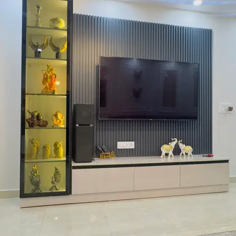 Living room with a fluted grey slat-panel TV wall, a tall backlit glass curio cabinet displaying brass figurines and religious idols