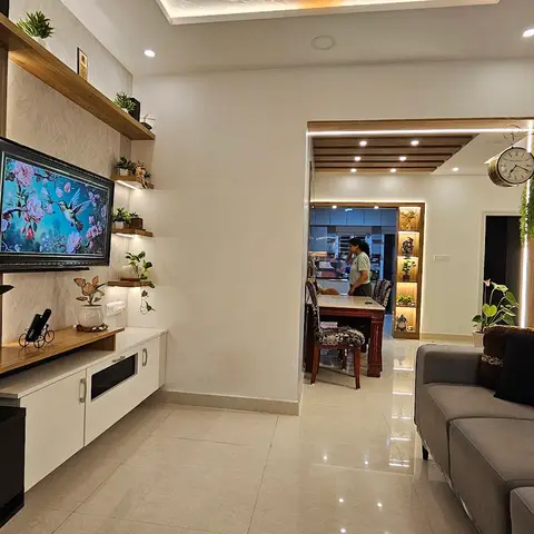 Living room with a fluted wood-panelled TV wall and floating shelves styled with plants, opening through an archway to the dining and kitchen beyond