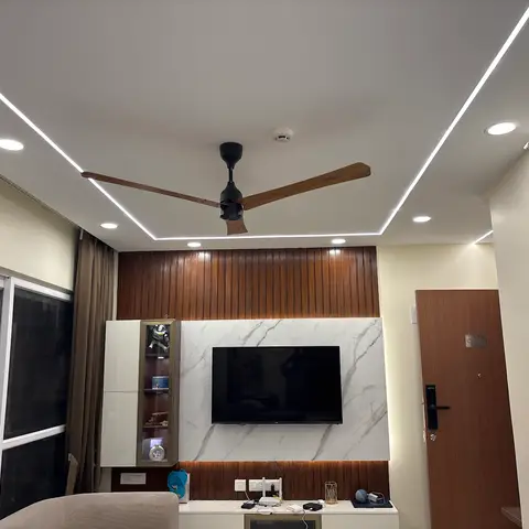 Living room with a fluted-wood and marble-clad TV feature wall, a profile-lit false ceiling and a glass-fronted crockery display unit beside it.