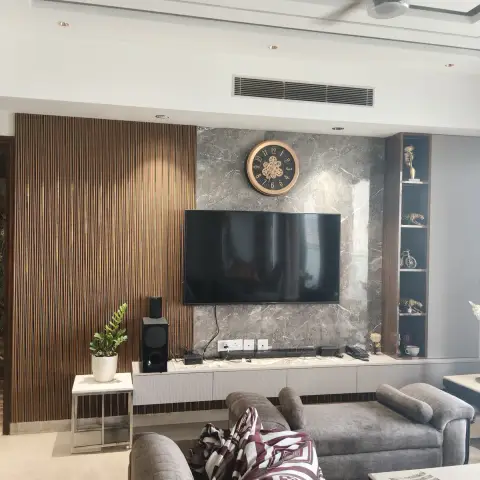 Living room with a fluted-wood and grey-marble TV feature wall, built-in display shelving with curios, and a grey sectional sofa with a patterned throw.