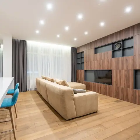 Living room with a full-height walnut veneer TV wall featuring open display niches, a beige sectional sofa on wide-plank wood flooring